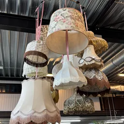 Verzameling van vintage hanglampenkappen met verschillende texturen en kleuren, opgehangen aan roze linten.