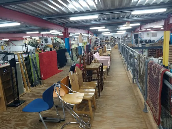 Winkelinterieur met houten stoelen, tafels en diverse meubels langs de zijkanten van een gangpad