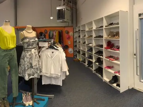 Winkelinterieur met kledingrekken, mannequins met kleding en witte stellingen met schoenen en accessoires