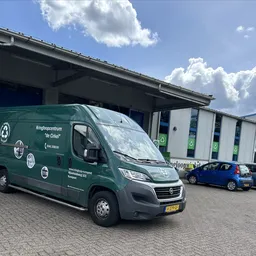 Groene bedrijfsbus met logo's en naam van kringloopcentrum geparkeerd op terrein