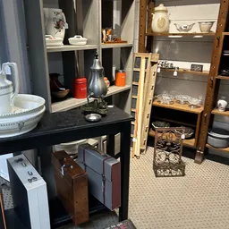 Winkelbinnenruimte met zwarte tafel, open kasten met serviesgoed, koppelingen en decoratieve items