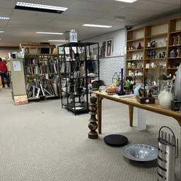 Winkelvloer met houten tafel, stellingen met decoratieve items, zwarte opbergrekken met gereedschap en kunstnijverheidsbenodi