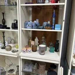 Witte stellingkast met decoratieve items: blauwe aardewerk, glazen flesjes, kopjes, kaarsen en diverse huishoudelijke spullen