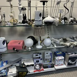 Stellingen met diverse huishoudelijke artikelen en lampen, waaronder roze gadget, witte bollen en andere gebruiksvoorwerpen
