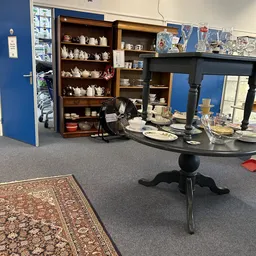 Winkelbinnenruimte met zwarte tafel met servies, houten wandkasten met theekannen en kopjes, blauwe wand en grijze vloer