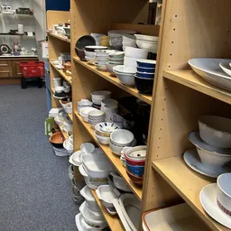 Houten stellingen vol met serviesgoed, borden, kommen en ander keukengerei in diverse kleuren en maten