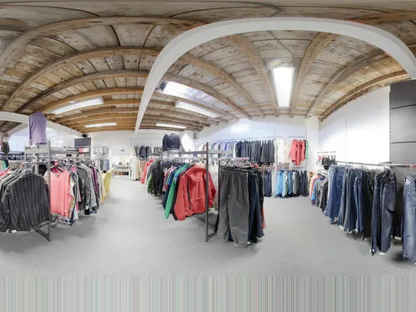 Ruim winkelinterieur met houten gewelfdak, rekken met tweedehands kleding in verschillende kleuren uitgstald