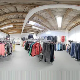Ruim winkelinterieur met houten gewelfdak, rekken met tweedehands kleding in verschillende kleuren uitgstald