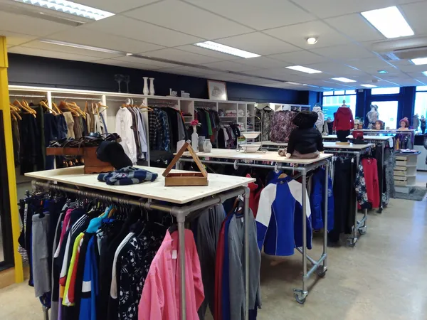 Winkelinterieur met rekken vol tweedehands kleding, tafels met uitgestalde spullen en kasten op de achtergrond