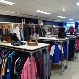 Winkelinterieur met rekken vol tweedehands kleding, tafels met uitgestalde spullen en kasten op de achtergrond