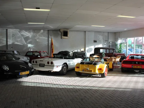 Showroom met verzameling klassieke en sportauto's, waaronder een witte Corvette en gele sportwagen