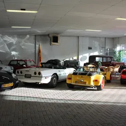 Showroom met verzameling klassieke en sportauto's, waaronder een witte Corvette en gele sportwagen