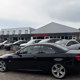 Zwarte BMW coupé op parkeerterrein van autobedrijf met andere auto's op achtergrond