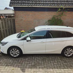 Witte stationwagen geparkeerd op oprit naast bakstenen garage