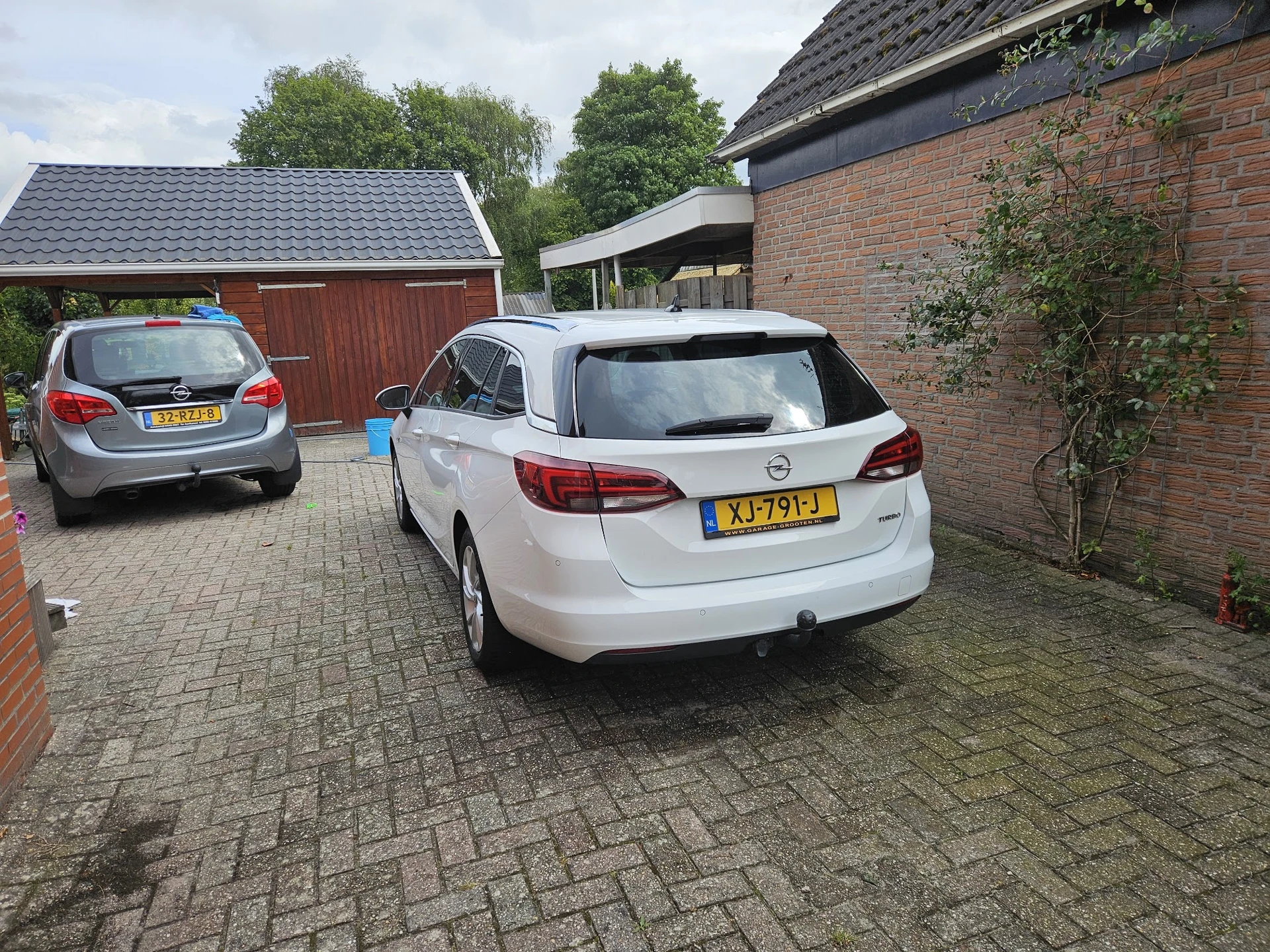Parkeerplaats met twee auto's naast een bakstenen garage met groene beplanting