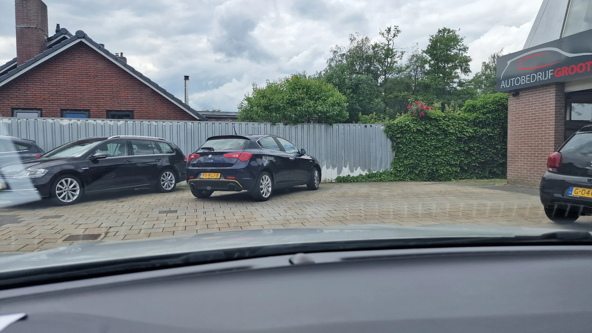 Parkeerplaats met enkele auto's en witte schutting, deel van garage zichtbaar