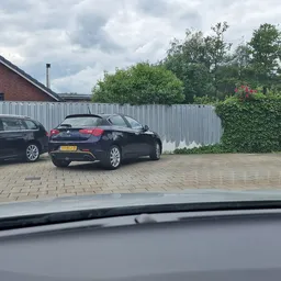 Parkeerplaats met enkele auto's en witte schutting, deel van garage zichtbaar