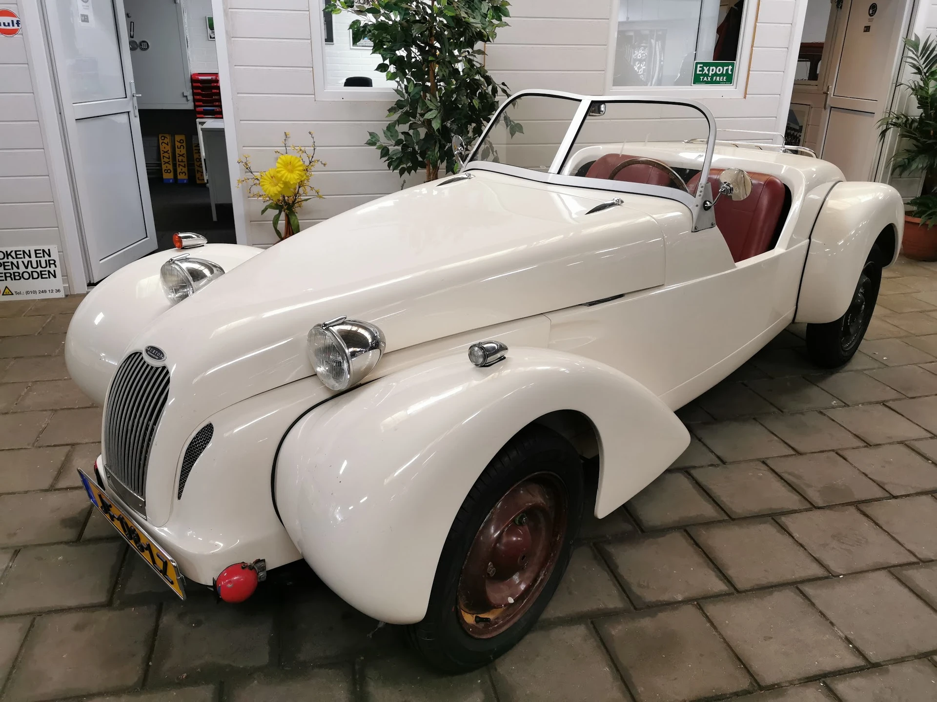 Witte vintage roadster uit de jaren 1940-1950 met rode stoelen, tentoongesteld in een garageinrichting