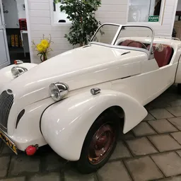 Witte vintage roadster uit de jaren 1940-1950 met rode stoelen, tentoongesteld in een garageinrichting