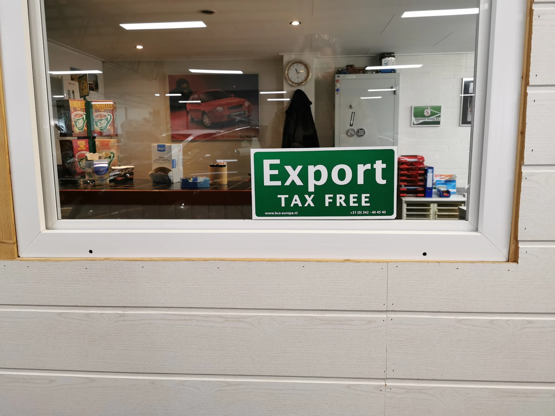 Winkelraam met groene 'Export Tax Free' sticker en uitzicht op winkelinterieur met schappen.