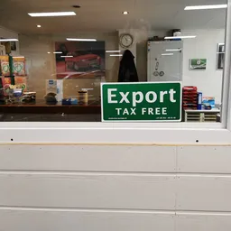 Winkelraam met groene 'Export Tax Free' sticker en uitzicht op winkelinterieur met schappen.