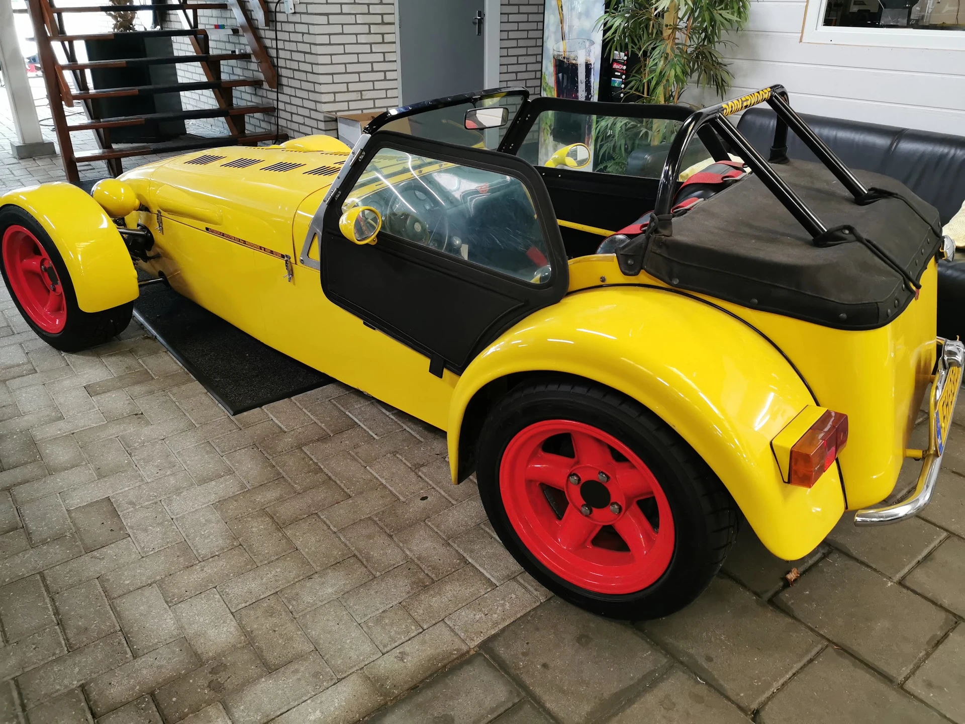Geel speelgoedautootje met zwarte interieur en rode wielen, geparkeerd op een tegelvloer