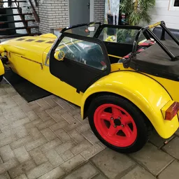 Geel speelgoedautootje met zwarte interieur en rode wielen, geparkeerd op een tegelvloer