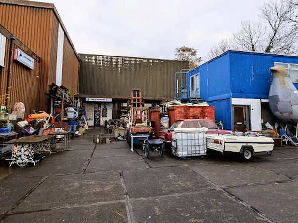 Bedrijfsterrein met drie gebouwen: bruin golfdak aan links, grijs metalen pand in midden, blauw onderkomen aan rechts, met di