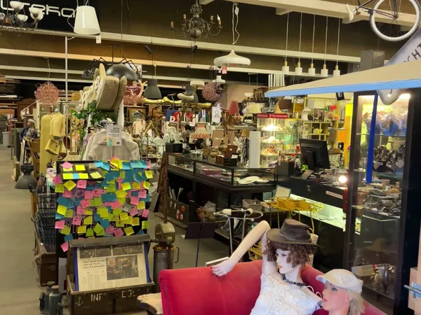 Interieur van kringloopwinkel met stellingen, diverse spullen, hang- en displayartikelen, klant zittend op rode stoel