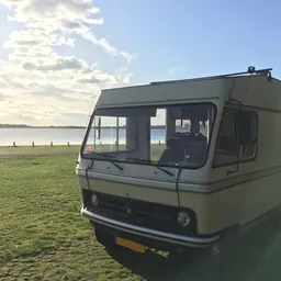 Groene camper of mobilhome geparkeerd op grasveld met water op achtergrond