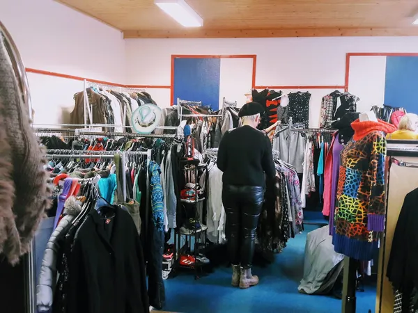 Winkelvloer van kledingwinkel met rekken vol tweedehands kleding, blauwe vloer en rode decoratieve elementen aan wand