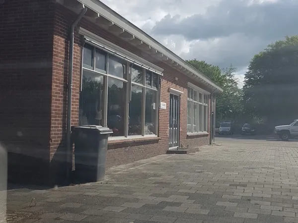 Voorgevel van een bakstenen winkel met grote ramen en ingang, gezien vanaf het plein