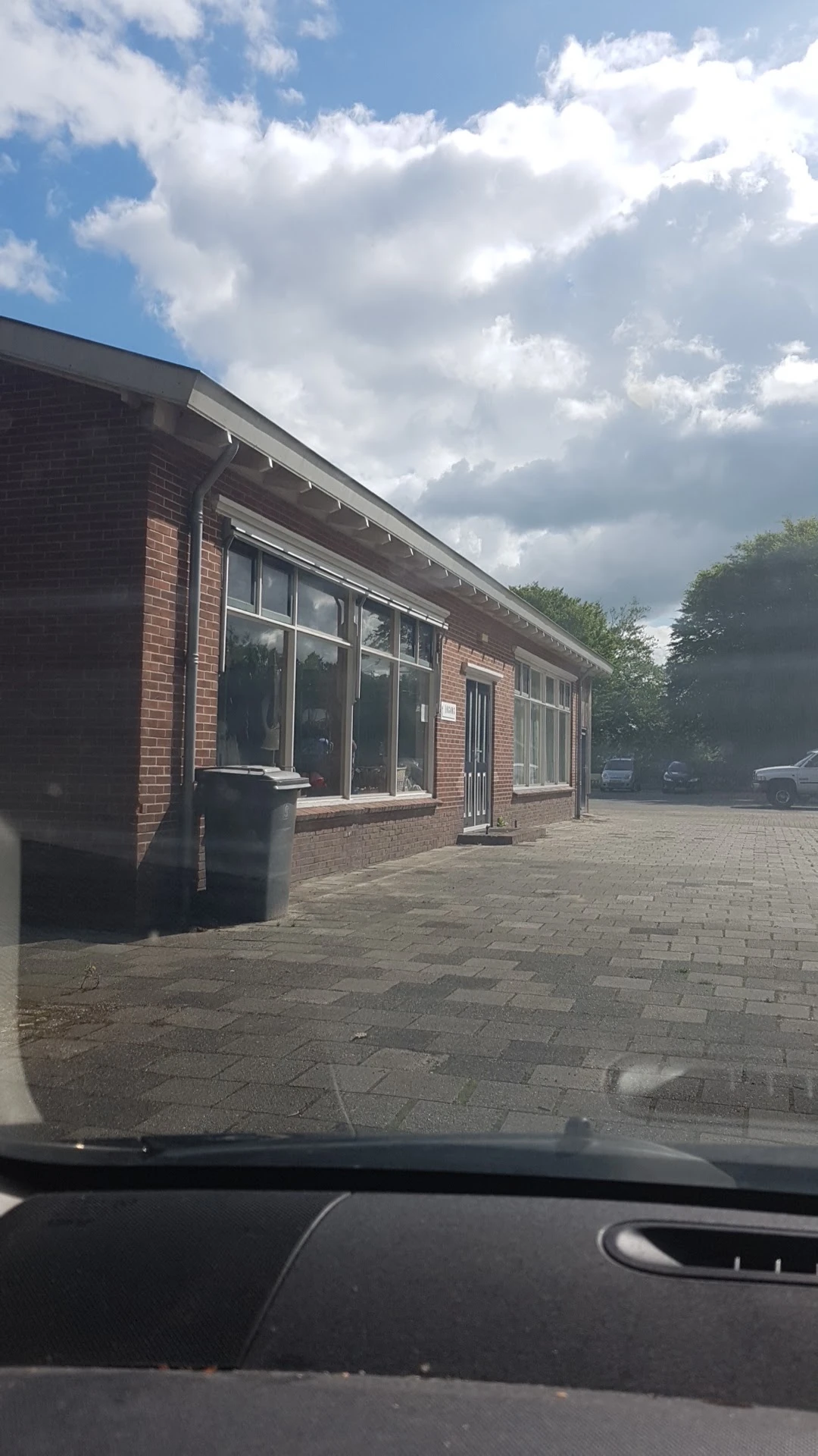 Voorgevel van een bakstenen winkel met grote ramen en ingang, gezien vanaf het plein