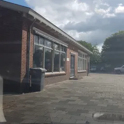 Voorgevel van een bakstenen winkel met grote ramen en ingang, gezien vanaf het plein