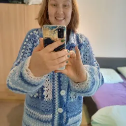 Spiegelselfie van een persoon in blauwe gebreide cardigan met telefoon