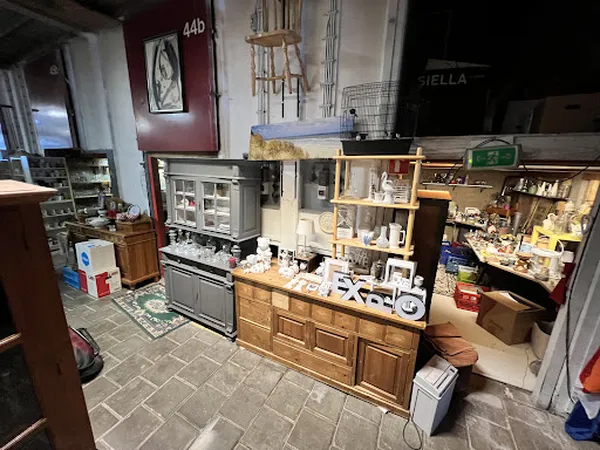 Winkelinterieur met houten meubels, vitrinekast, stellingen met diverse spullen en grijze tegelvloer