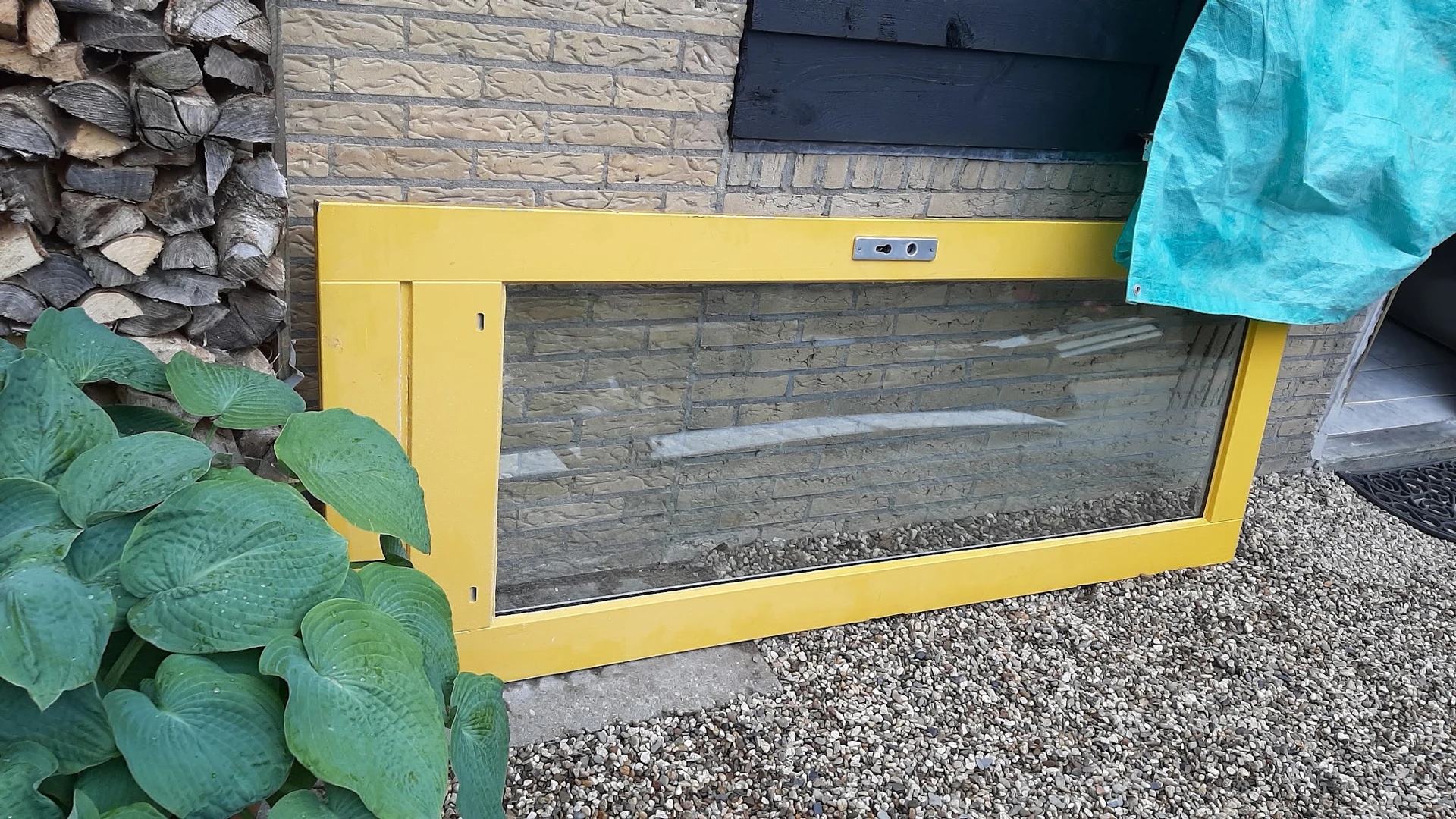Gele rechthoekige kist of bak met glazen voorkant, geplaatst tegen bakstenen muur