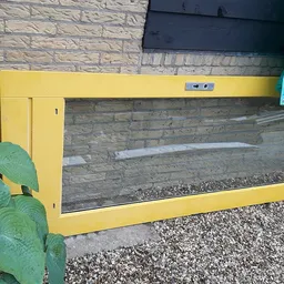 Gele rechthoekige kist of bak met glazen voorkant, geplaatst tegen bakstenen muur