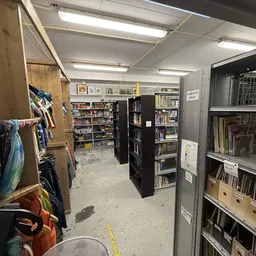 Winkelinterieur met stellingen vol boeken, dvd's en kleding aan hangers langs de wanden