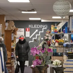 Interieur van kringloopwinkel met kleding, decoratie en huishoudspullen op stellingen en display tegen donkere wand met 'KLED