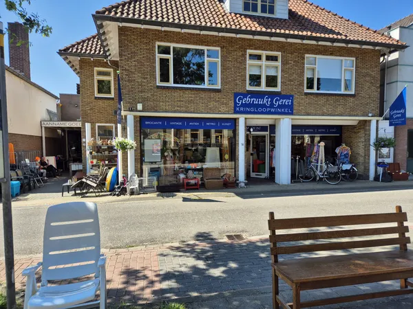 Voorgevel van kringloopwinkel Gebruukt Gerei met blauwe winkelruit, twee deuren en fietsen ervoor