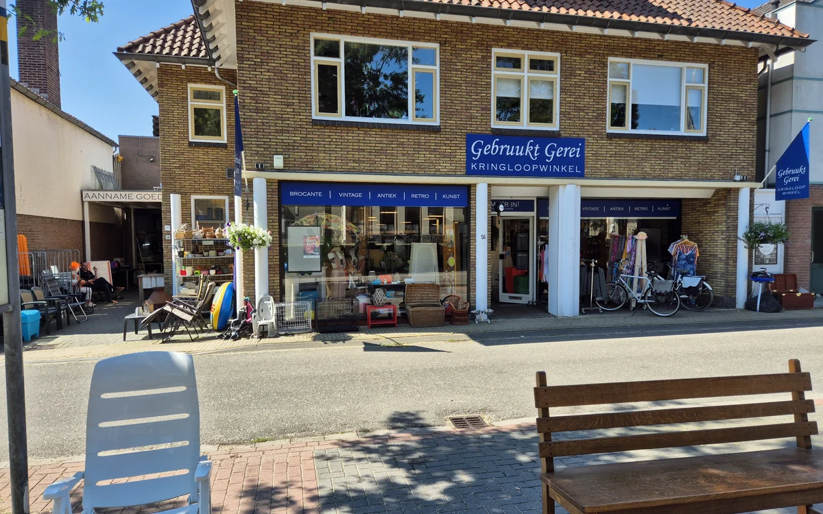 Voorgevel van kringloopwinkel Gebruukt Gerei met blauwe winkelruit, twee deuren en fietsen ervoor