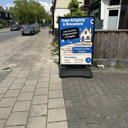 Straatgevel met blauw winkelbordje voor Gema-Kringloop & Brocanterie, openingstijden zichtbaar