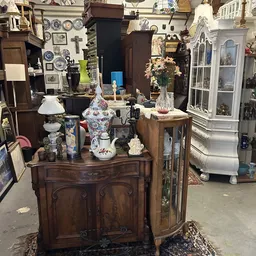 Houten kasten en diverses huisraad met lampen, vazen, servies en decoratieve spullen in een kringloopwinkel