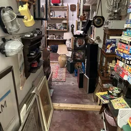 Smal gang tussen stellingen met boeken, speelgoed en huishoudspullen in een kringloopwinkel