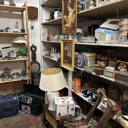 Stellingen met diverse huishoudartikelen, lampen, servies, gereedschap en decoratieve spullen in een kringloopwinkel