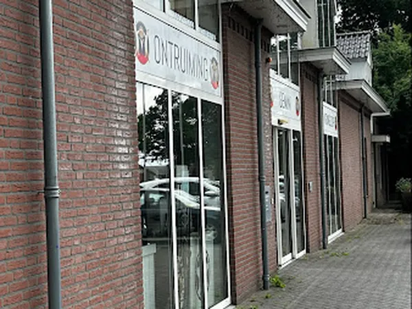 Gevel van kringloopwinkel met glazen deur en witte uithangbord, rode bakstenen muur en stoeprand
