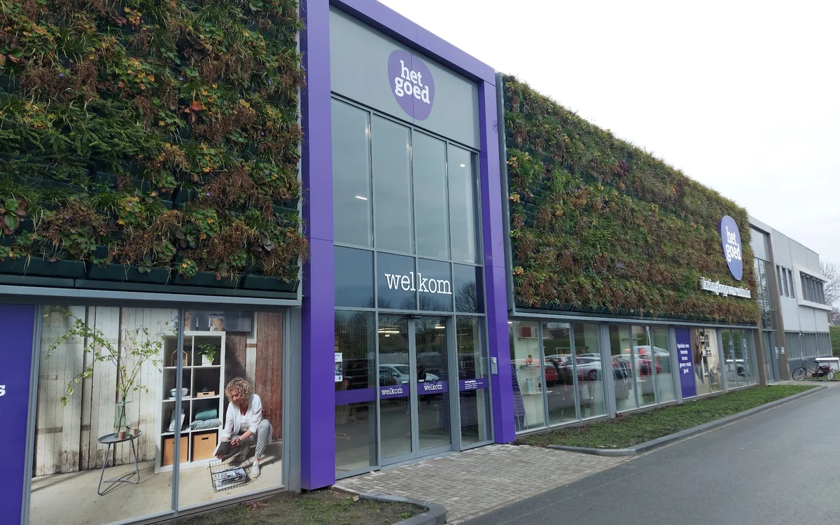 Voorgevel van kringloopwinkel met paarse pui, glazen deuren en groene gevelbeplanting