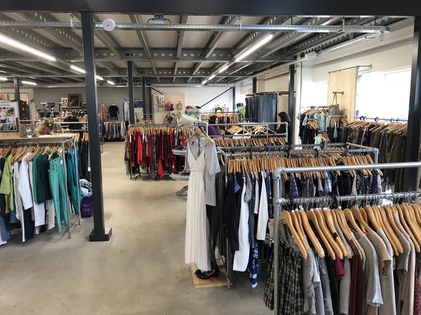 Winkelvloer met meerdere rekken vol tweedehands kleding op hangers, stellingen en industrieel plafond