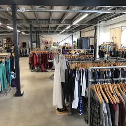 Winkelvloer met rekken vol tweedehands kleding op houten hangers, industrieel plafond met verlichting